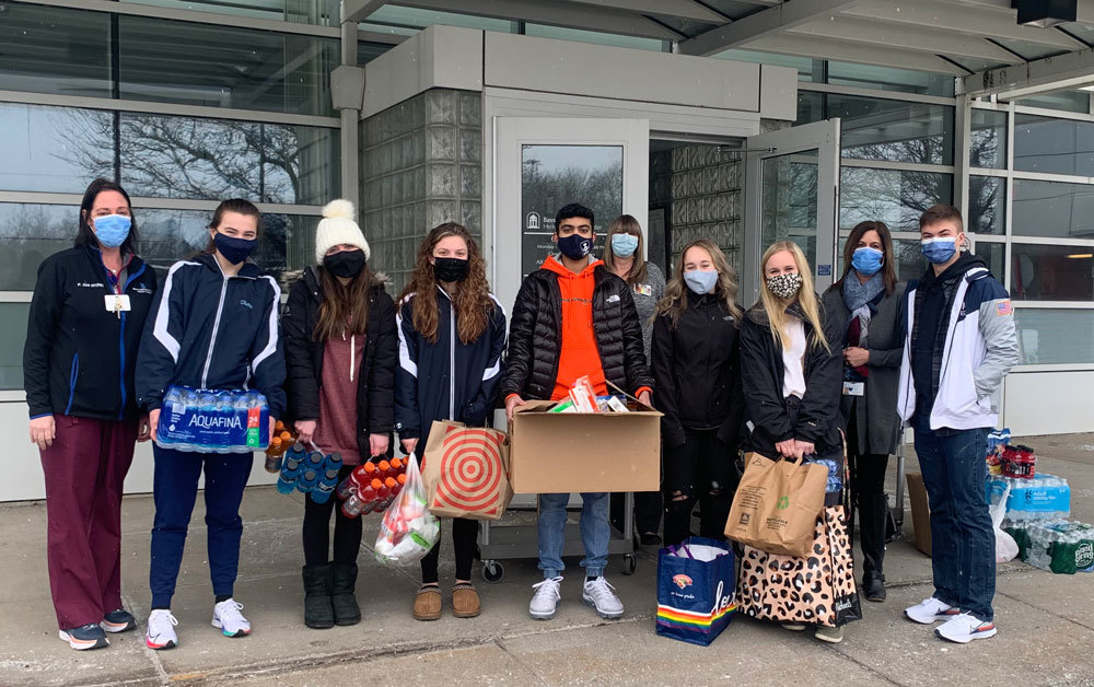 Outdoors, 10 people in coats and masks,  holding boxes and bags