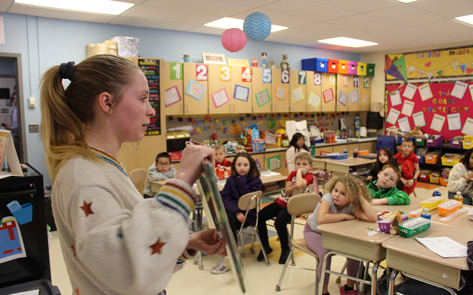 Girl holding a book in a class, young students at desks