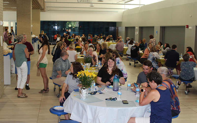 cafeteria filled with people, seated, standing, tablecloths