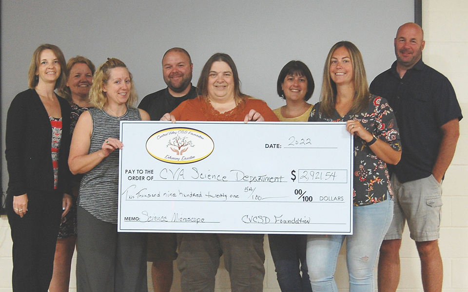 8 people standing, smiling, giant check