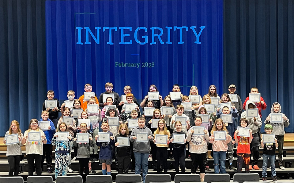 group of students holding certificates standing on risers in front of giant word "integrity"