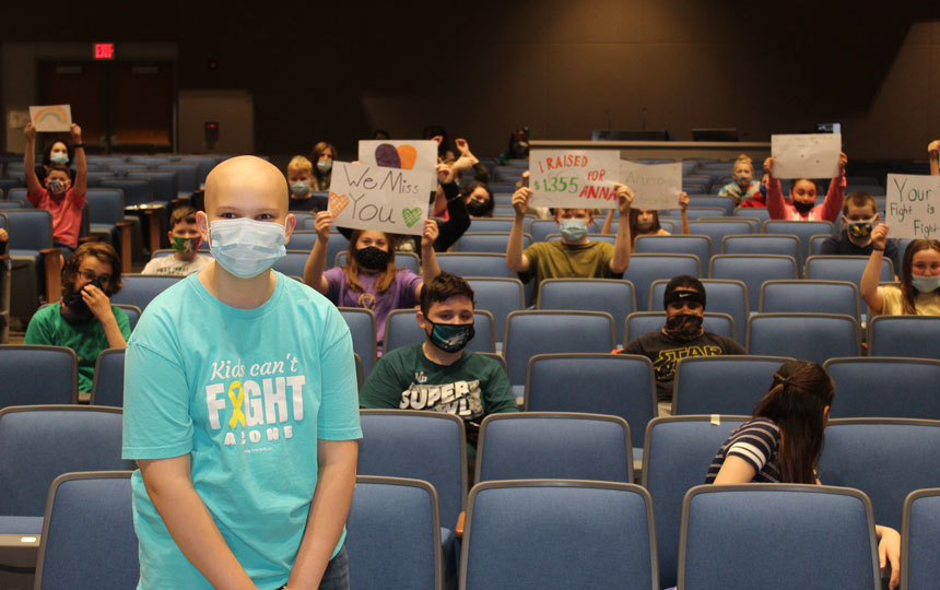girl in mask background of students in auditorium seats holding signs