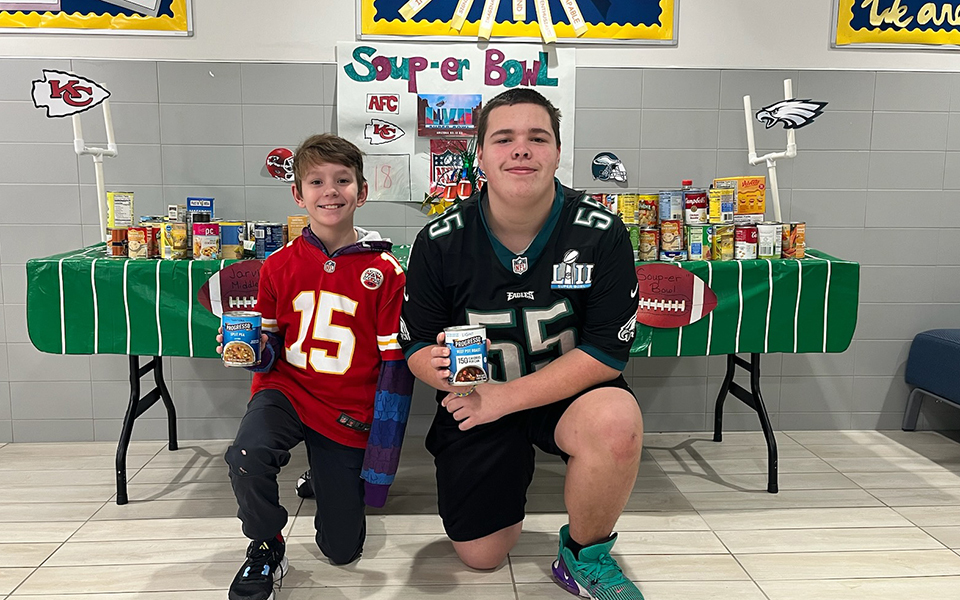 2 boys wearing team jerseys and kneeling in front of a table decorated like a football field