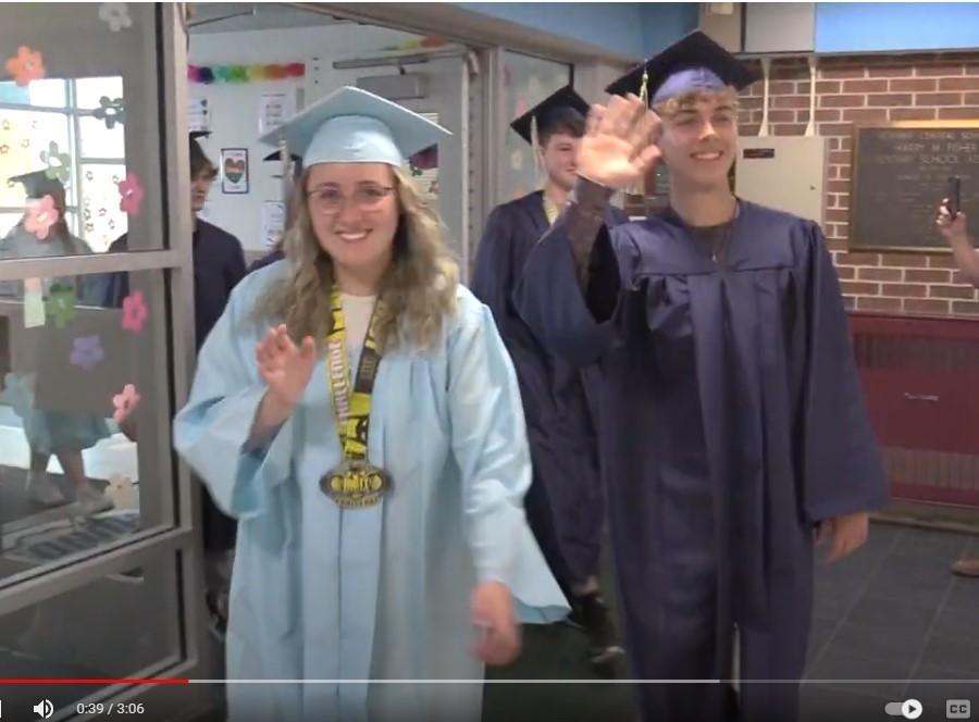 students wearing caps and gowns walk through glass doors, waving