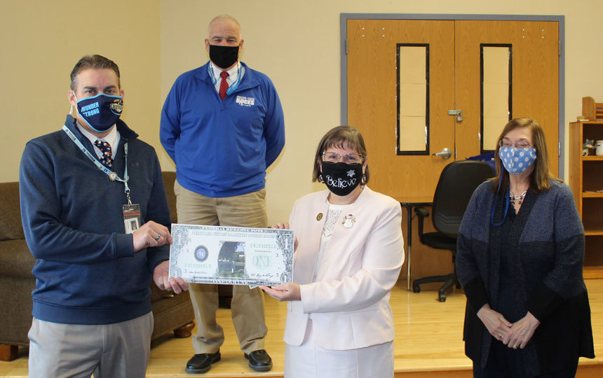 4 people indoors, two holding giant dollar bill