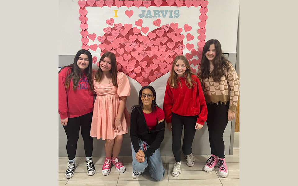 5 girls posing in front of big heart covered with smaller hearts