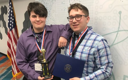 two young men, whiteboard, U.S. flag, trophy, medallions