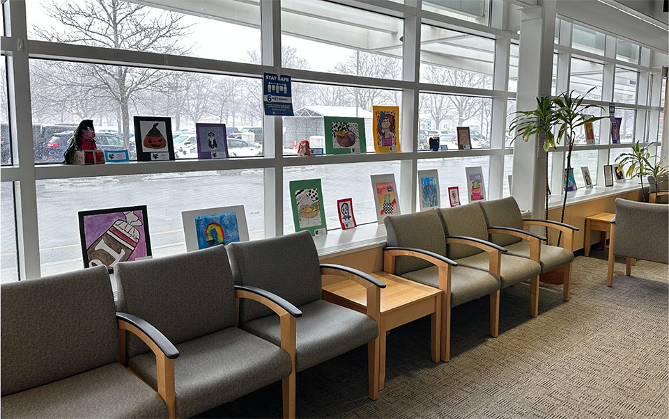 art displayed in large bank of windows behind row of chairs