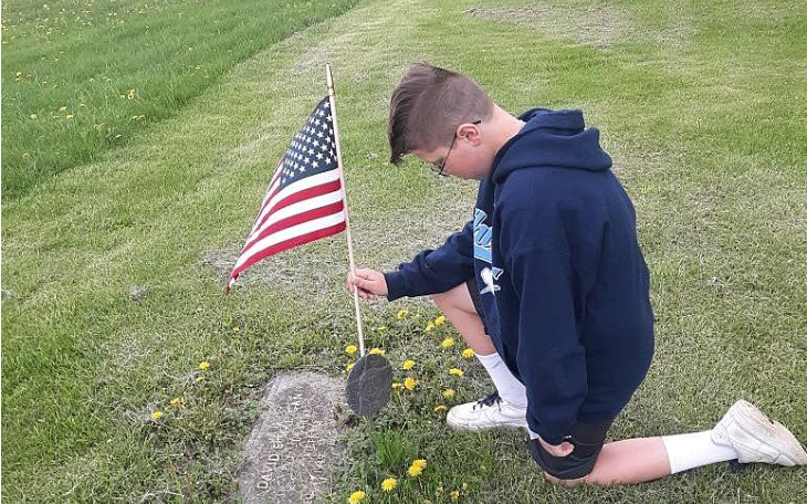 boy on one knee placing U.S. flag on grave