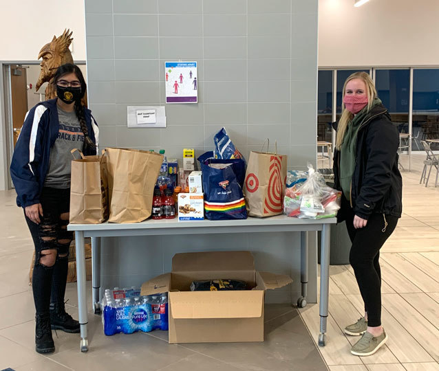 2 people indoors, masks, table filled with bags and boxes