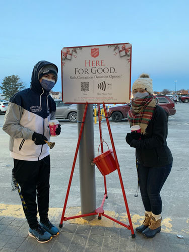 2 people outdoors, masked, winter clothes, Salvation Army kettle