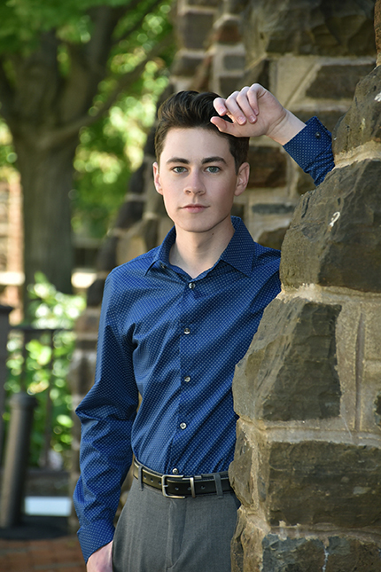 young man outdoors, leaning on stone wall