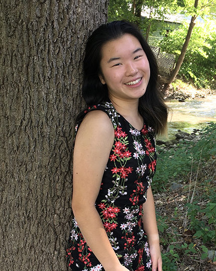 young lady outdoors, leaning with back against tree