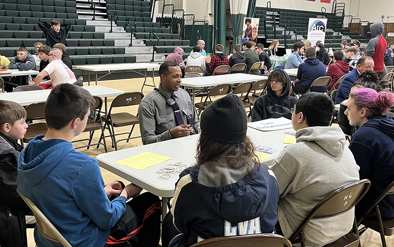 gymnasium, students and adults seated at tables, speaking