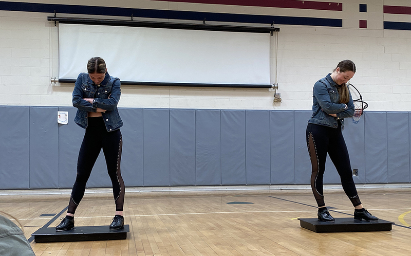 two dancers apart, arms folded in gym