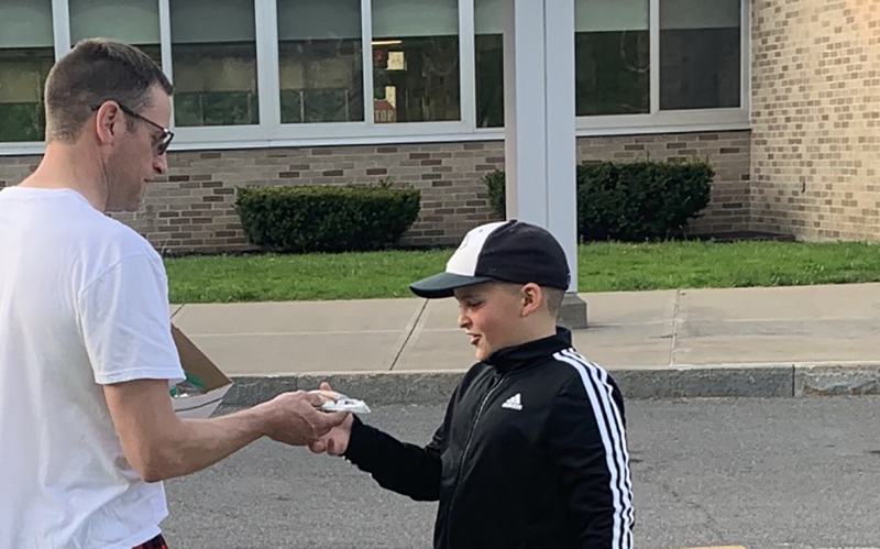 man handing goodie bag to boy in cap, outdoors, grass, school