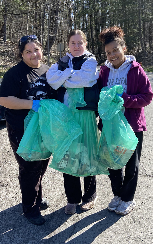 three girls outside holding trash bags