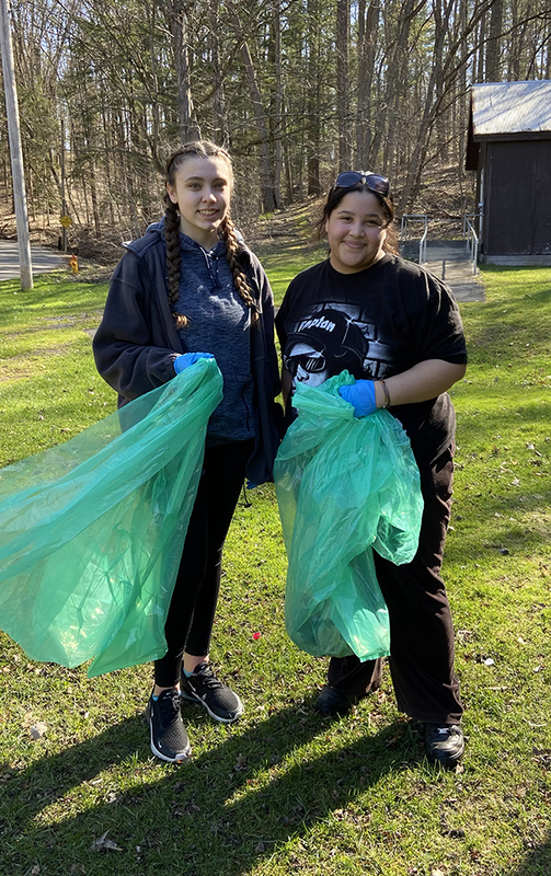 2 girls outside with trash bags, grass, trees