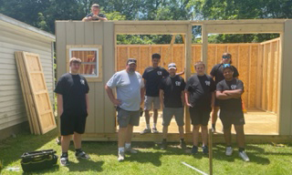 group of students, outdoors, partially built shed, grass