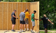 paritally constructed shed, six people, trees, grass