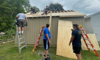 three people, partially constructed shed, two ladders, trees, grass