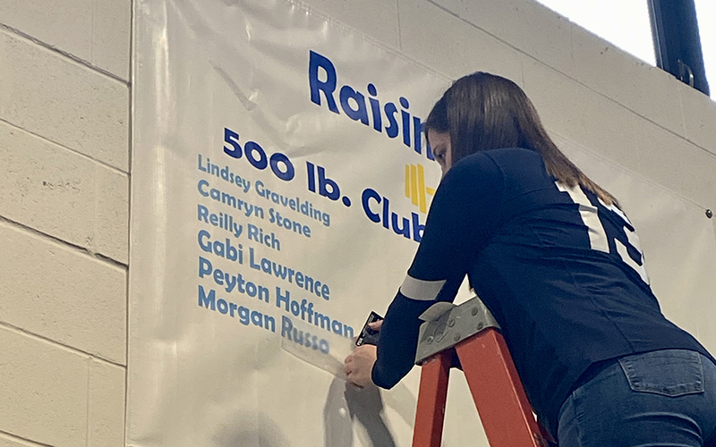 Girl on ladder adding name to a poster