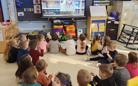 small chidren seated on floor, watching large TV, classroom