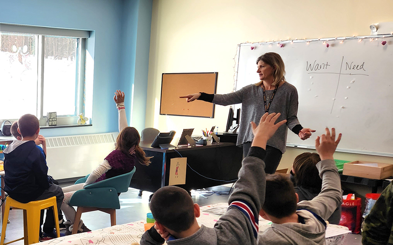 Adult calling on student in classroom, children, desks, whiteboard, window