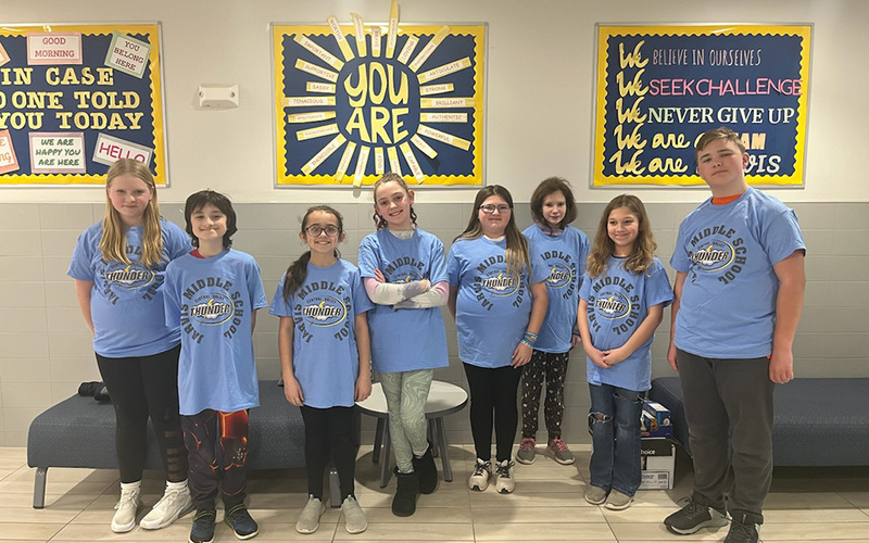 8 smiling students wearing same t-shirts, standing
