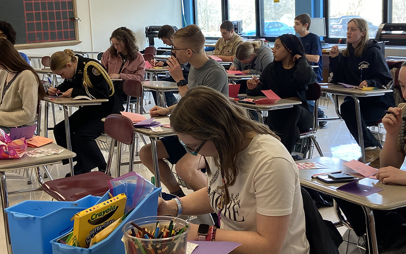 classroom filled with students at desks, making cards, windows