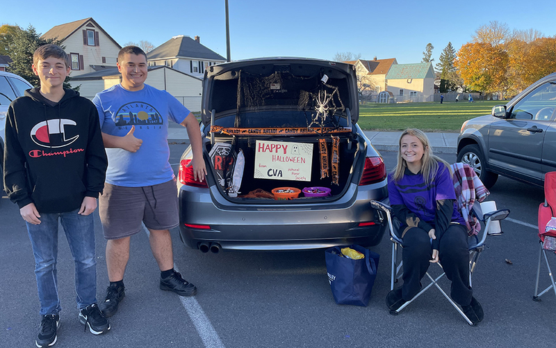 4 students, car with trunk open, candy in back, happy halloween sign