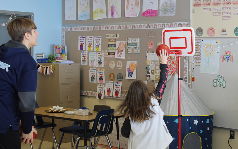 classroom, girl shooting mini basketball, desks, bulletin board
