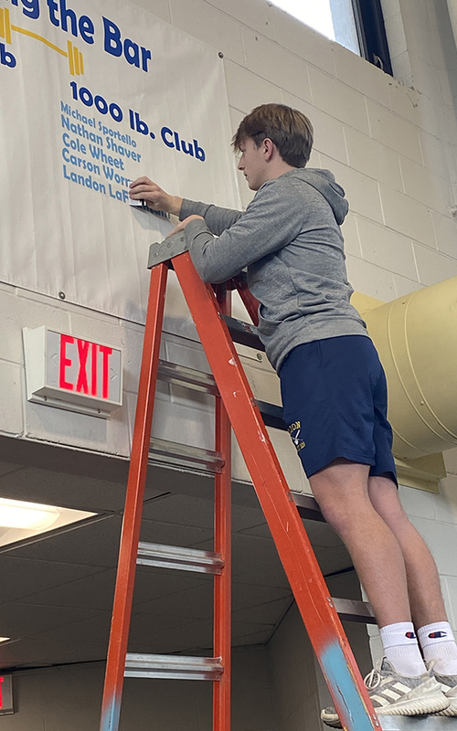 young man on ladder placing name on banner