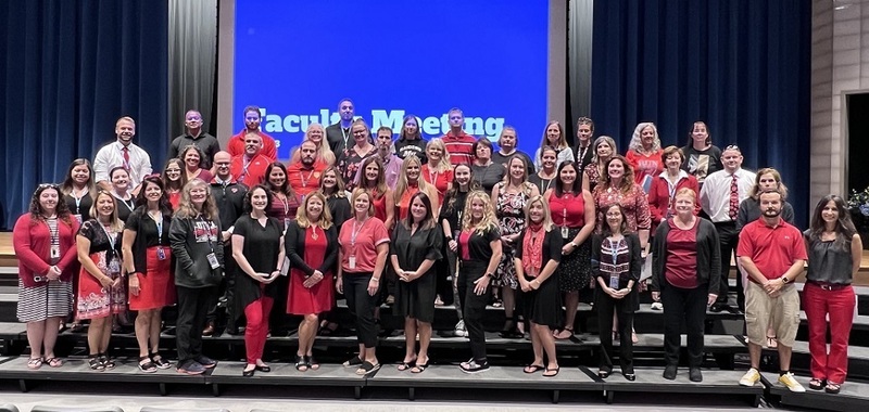 large group of teachers and staff standing on auditorium risers