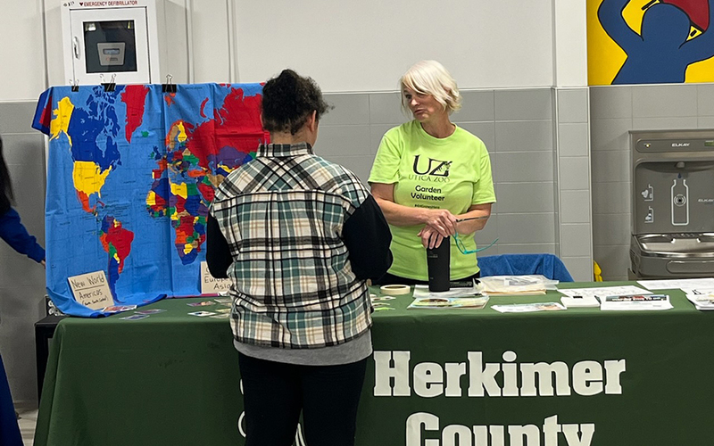 2 women talking at draped table with herkimer county sign, map display on table